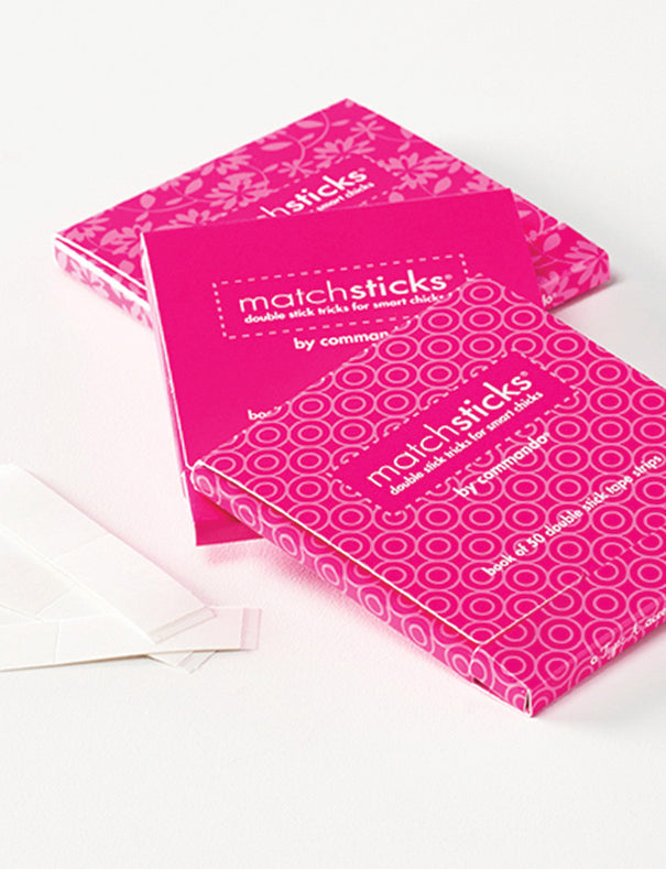 Two bright pink matchstick boxes with white circular patterns and a few loose white matchsticks on a clean white surface. The front box shows the visible brand text 'matchsticks by commando'.