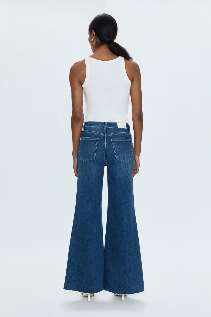 Person wearing blue flared jeans and a white top on a light gray background