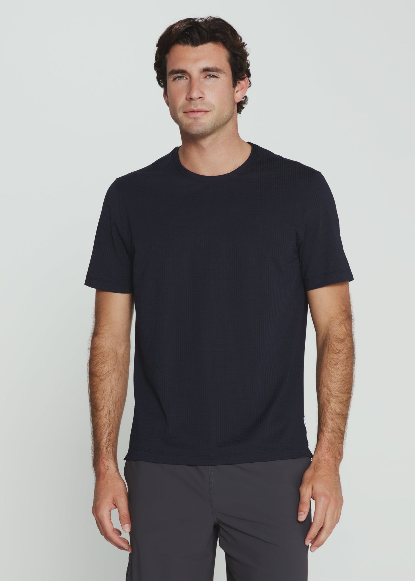 Man wearing a navy t-shirt and gray pants against a plain background