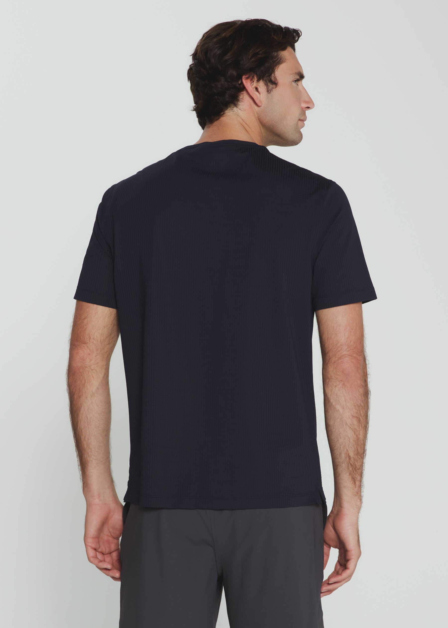 Man wearing a black polo shirt and gray pants against a white background