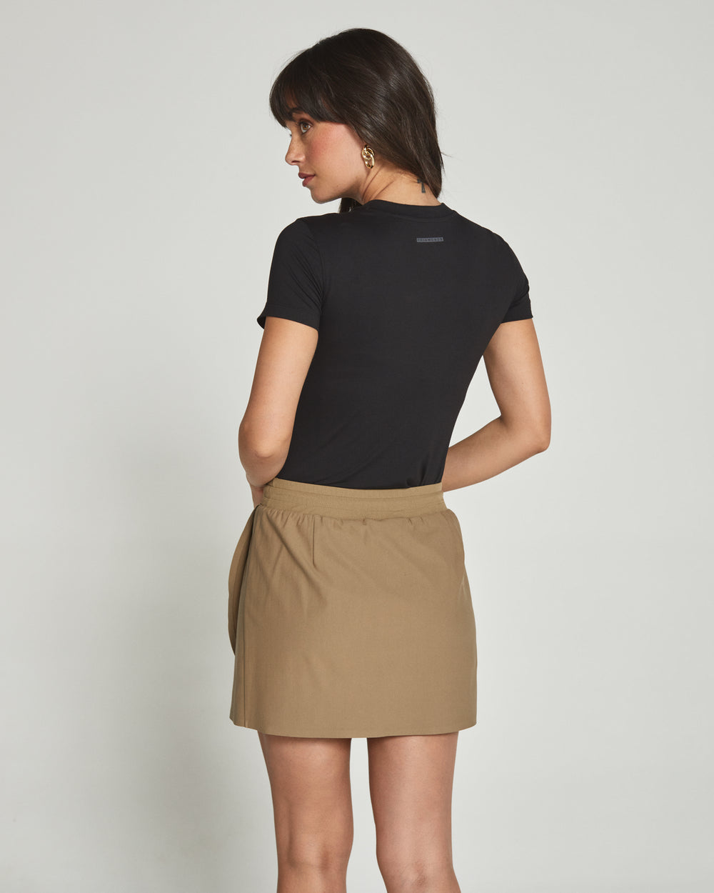Woman wearing a black top and beige skirt on a plain background