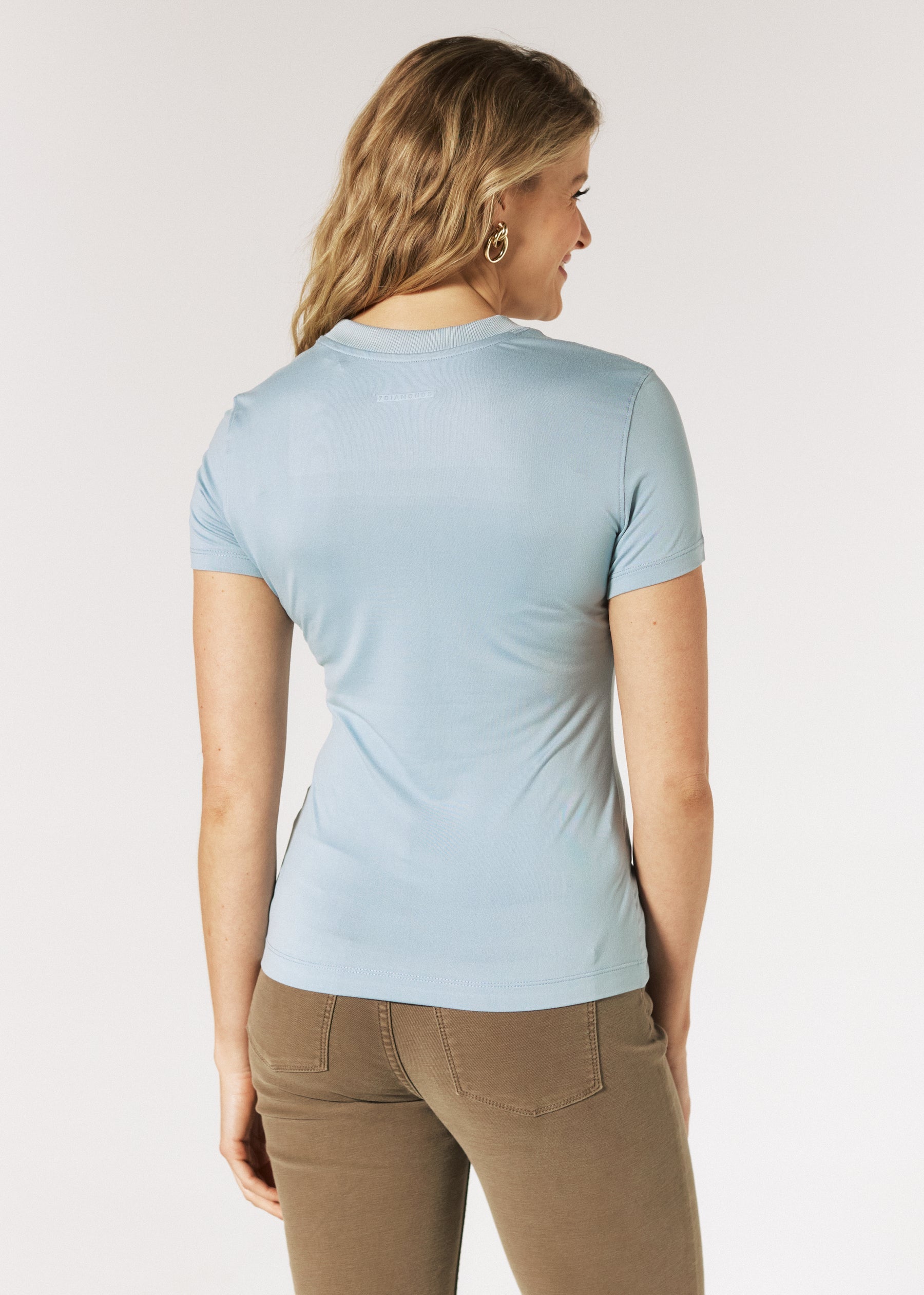 Woman wearing a blue ash top and beige pants on a plain background
