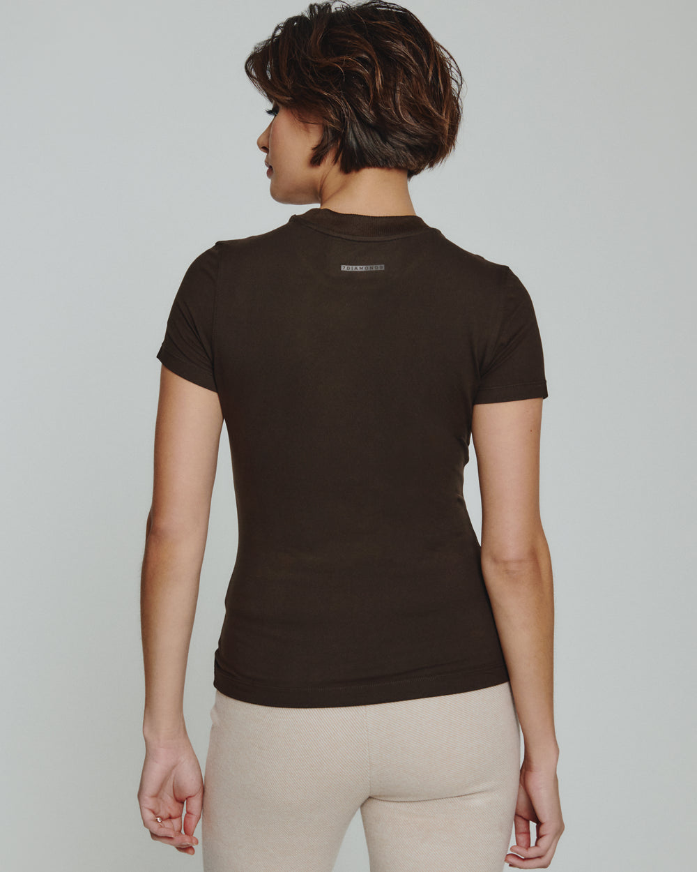 Person wearing a brown t-shirt with a logo on the back against a plain background