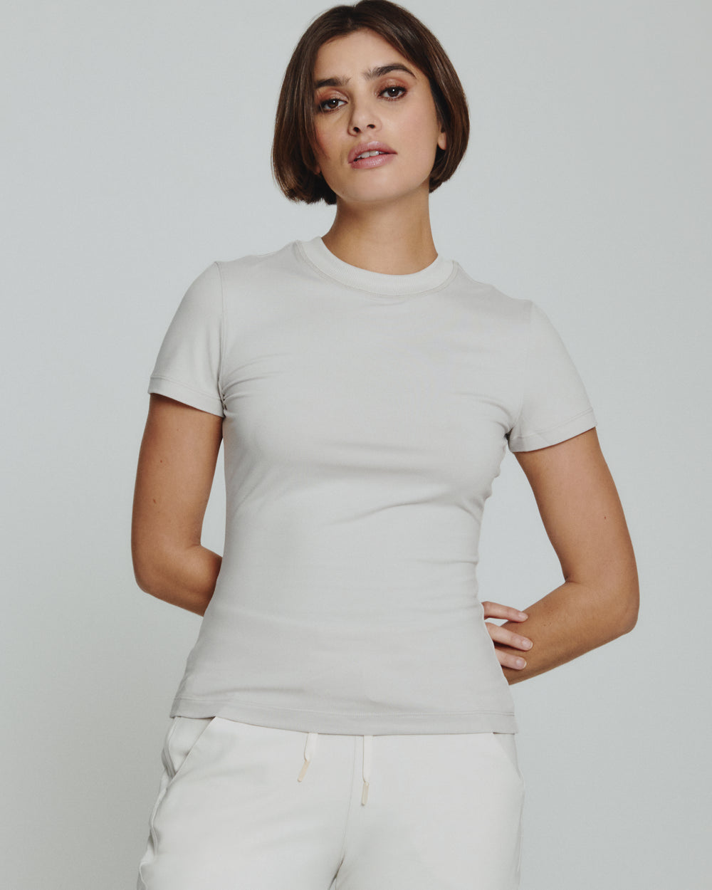 Woman wearing a light gray t-shirt and white pants against a plain background