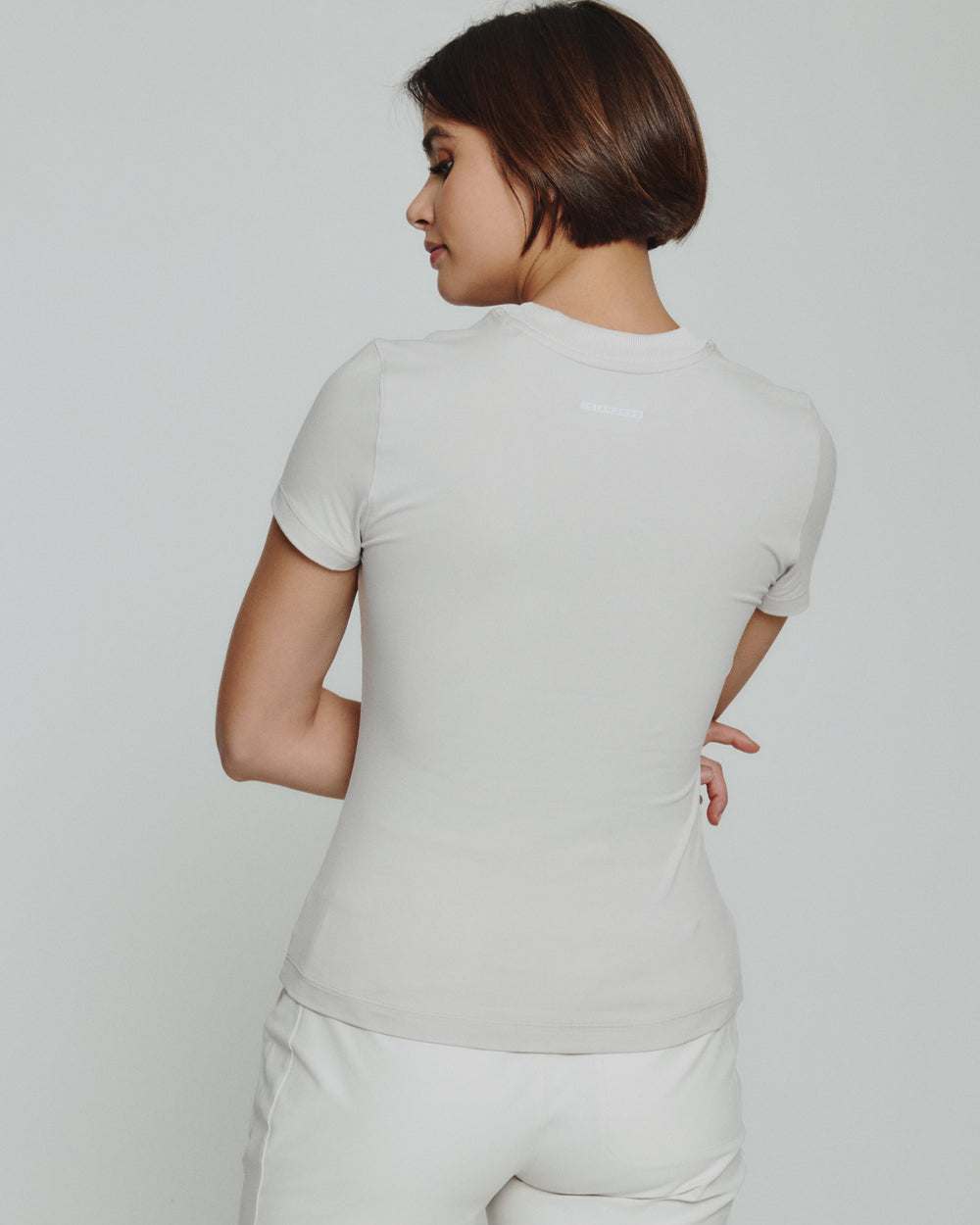 Woman wearing a light gray t-shirt and white pants against a plain background