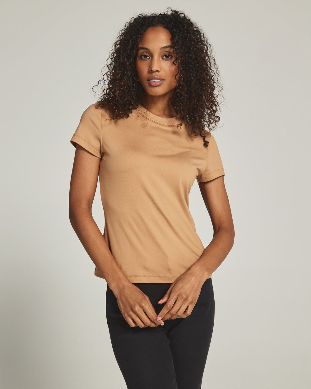 Woman wearing a beige t-shirt and black pants against a plain background
