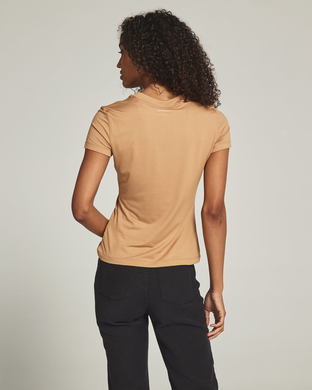 Person wearing a beige t-shirt and black pants against a plain background