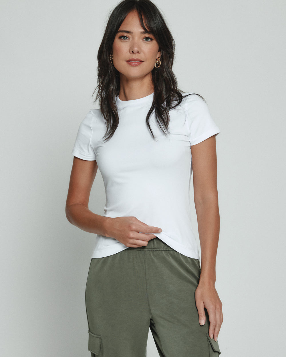 Woman wearing a white t-shirt and green pants against a plain background