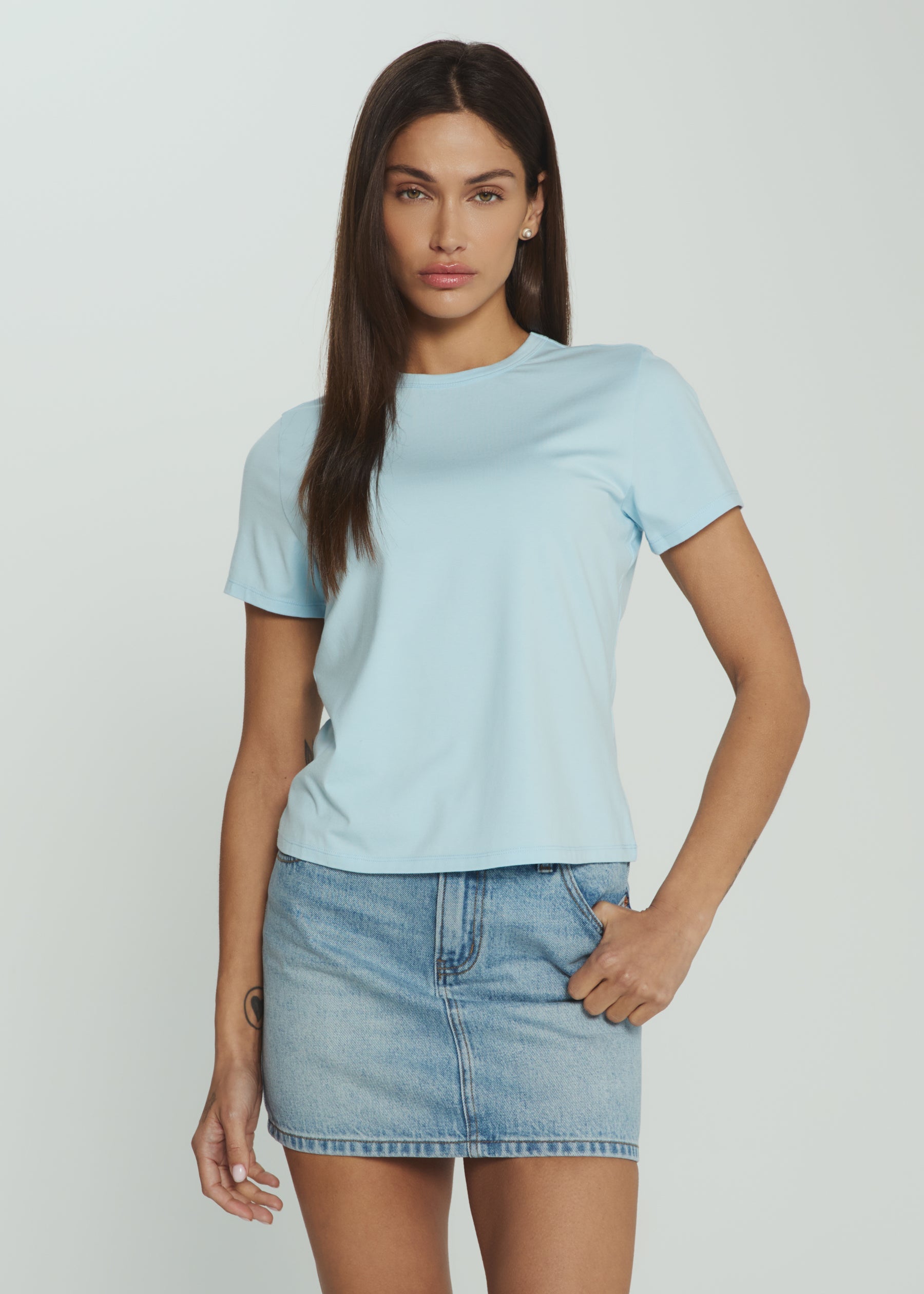Woman wearing a light blue t-shirt and denim skirt on a plain background