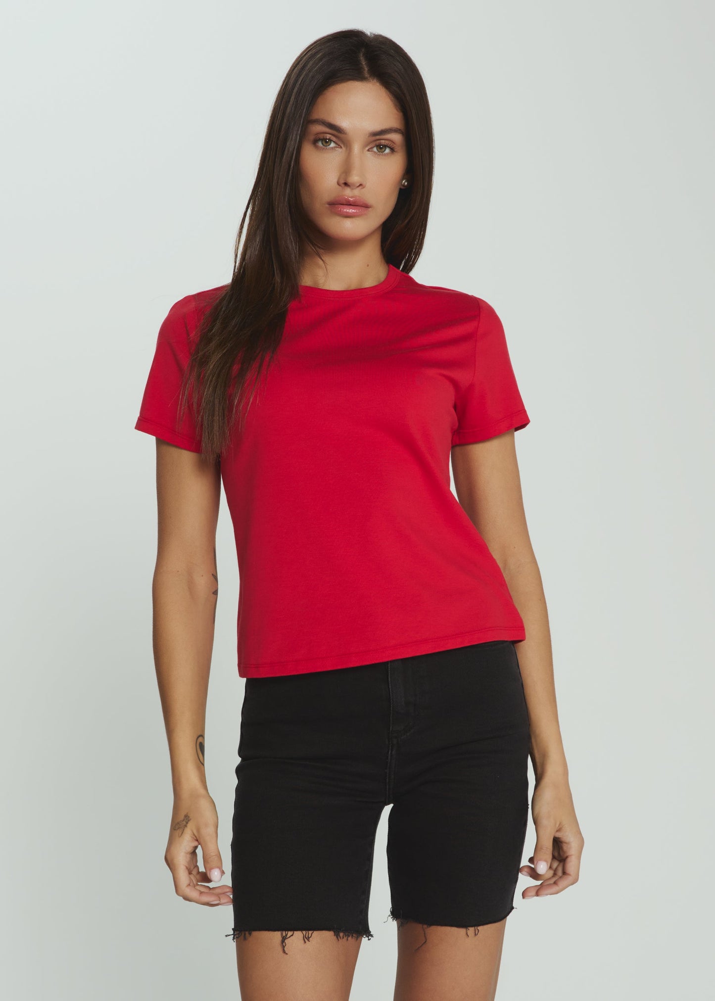 A woman modeling a bright red short-sleeve crewneck t-shirt paired with black denim shorts, set against a plain light gray studio background.