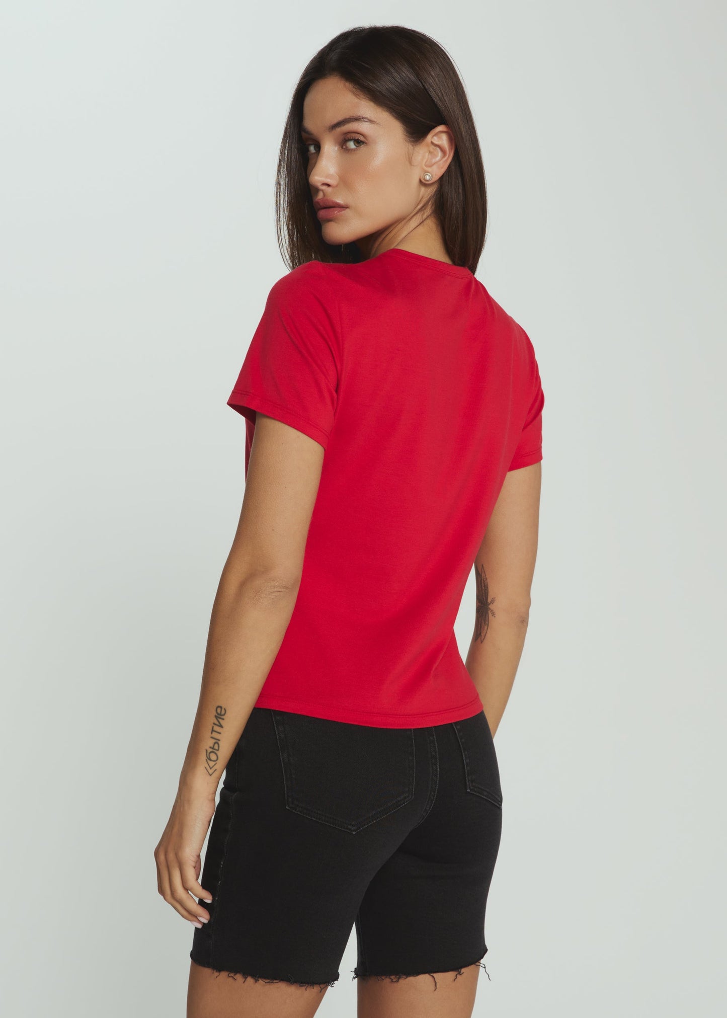 Woman wearing a red t-shirt and black shorts on a plain background