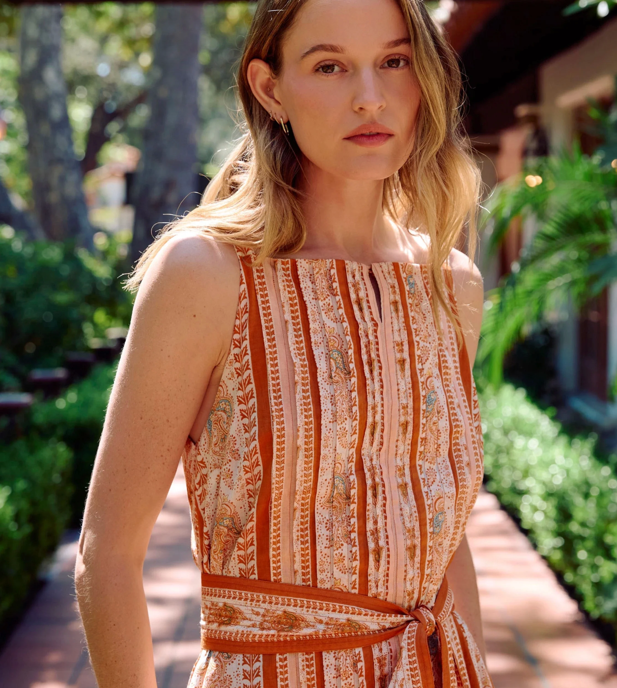 Woman wearing a patterned dress outdoors with greenery in the background
