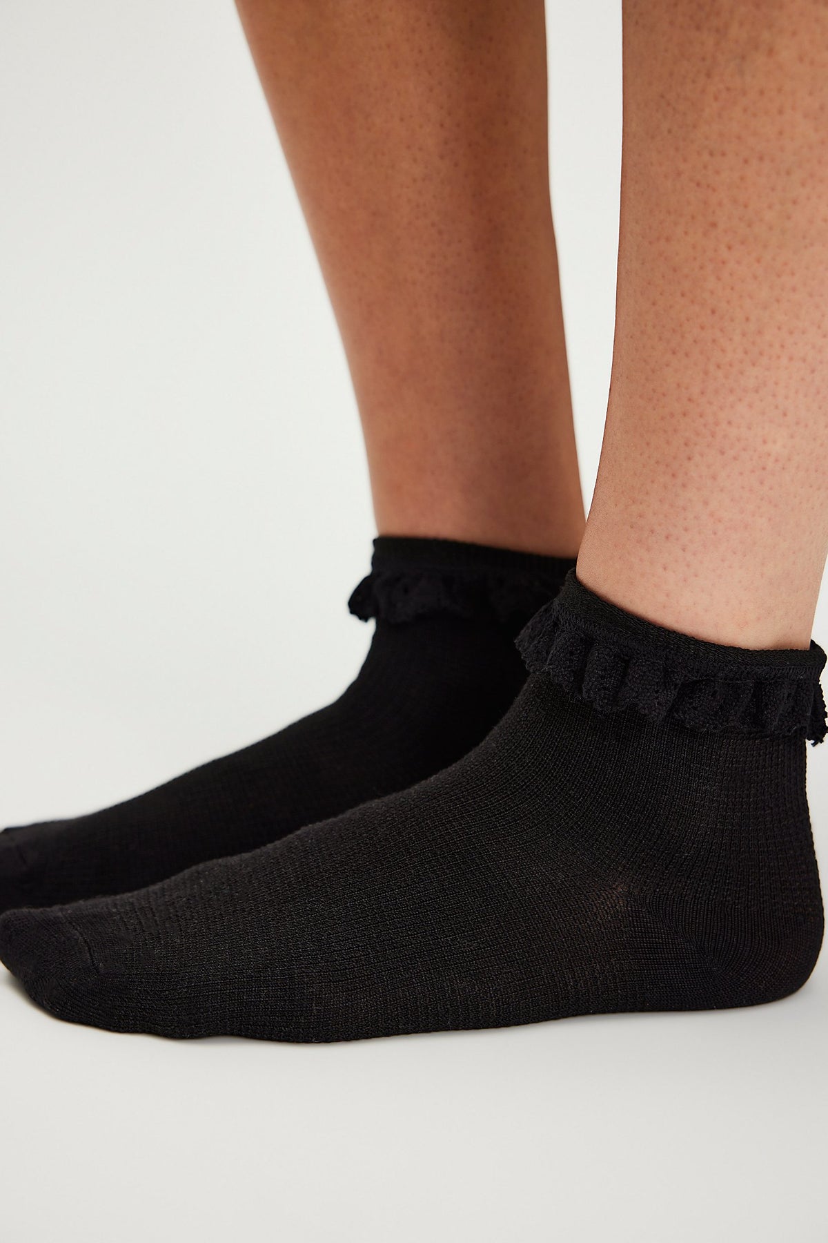 Black ankle socks with ruffles worn by a person on a white background