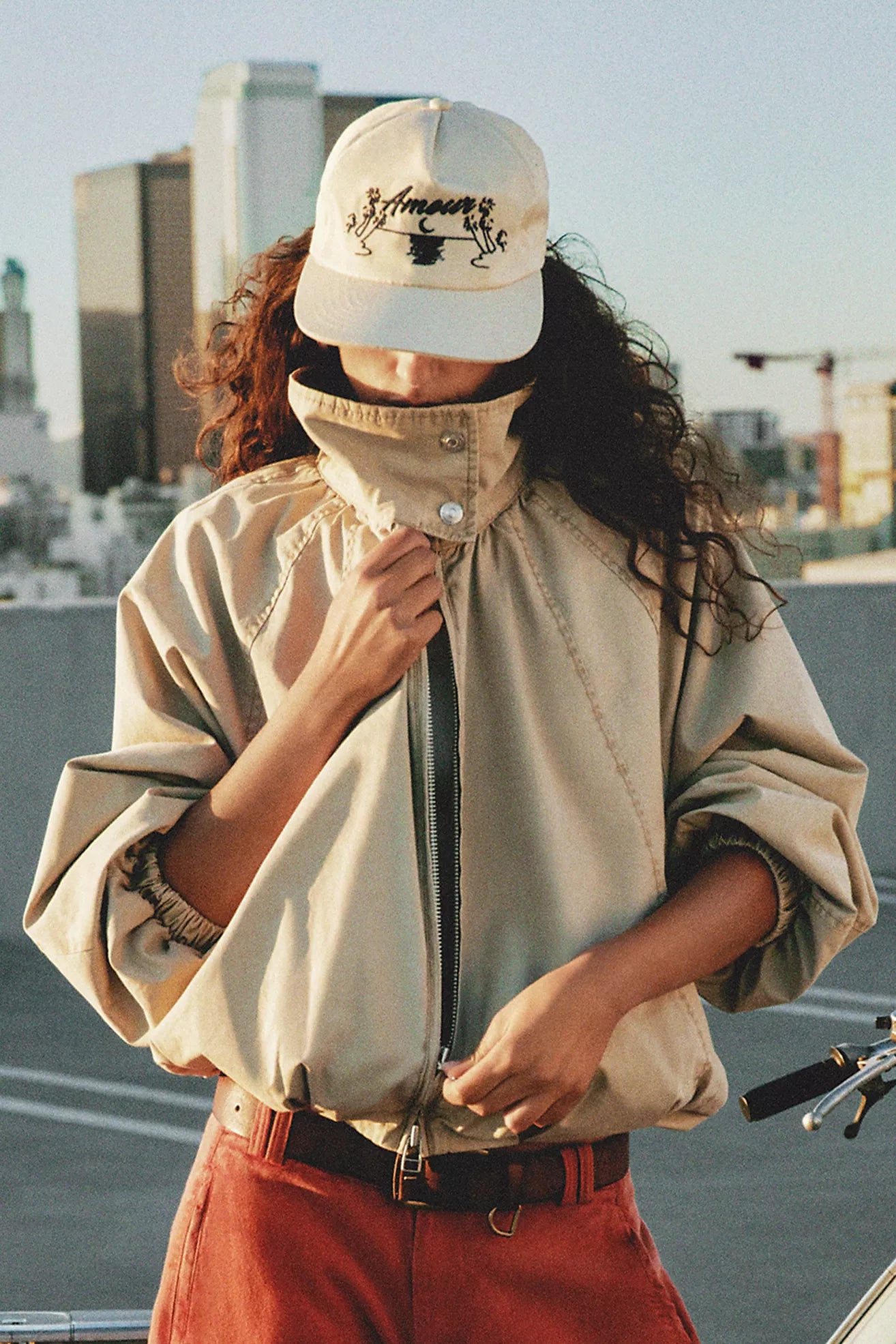Person wearing a beige jacket and red pants with a cityscape background