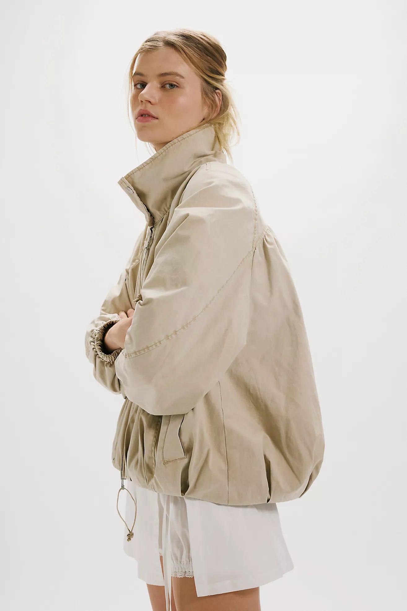 Woman wearing a beige jacket and white shorts on a white background