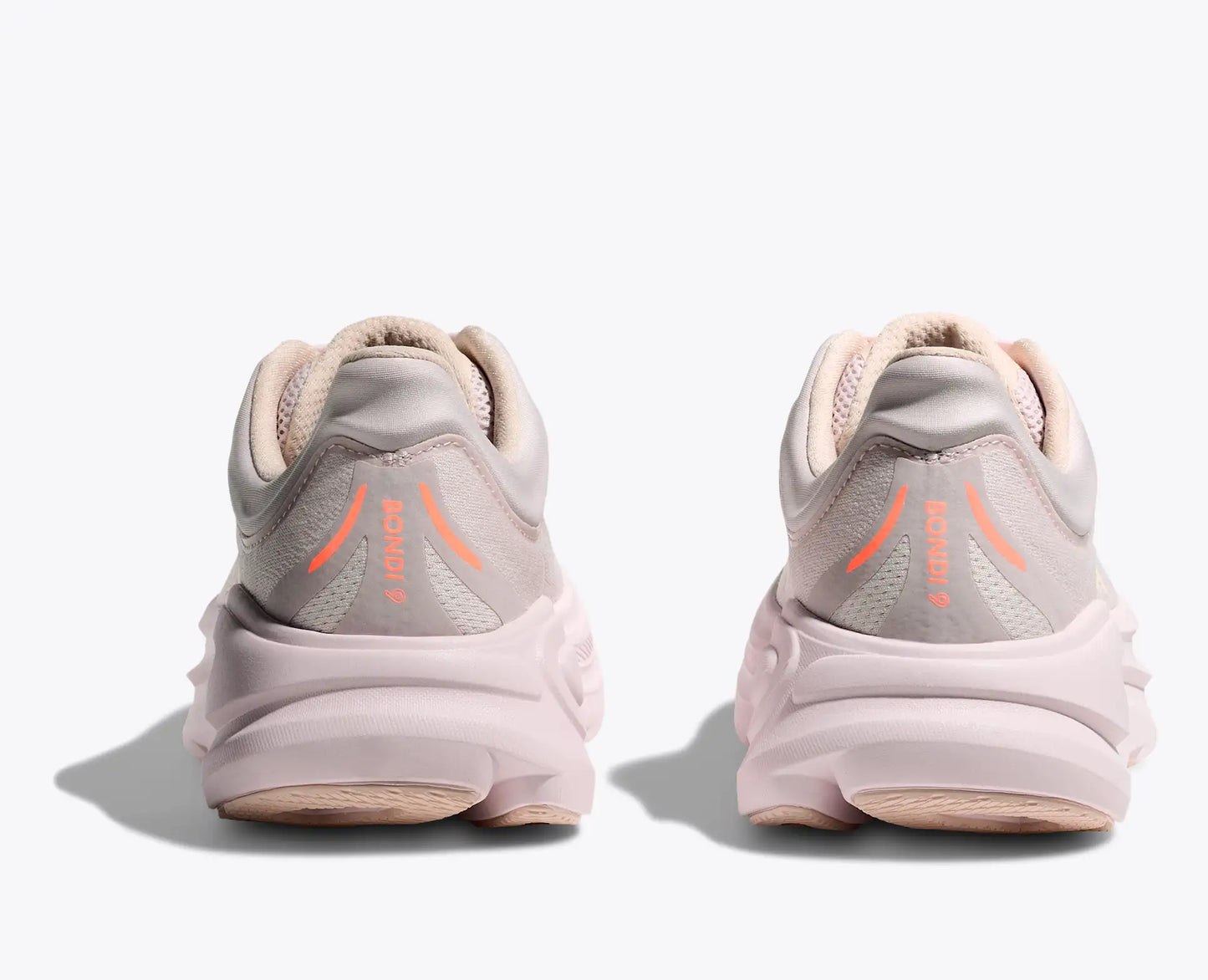 Pair of light pink running shoes with orange accents on a white background