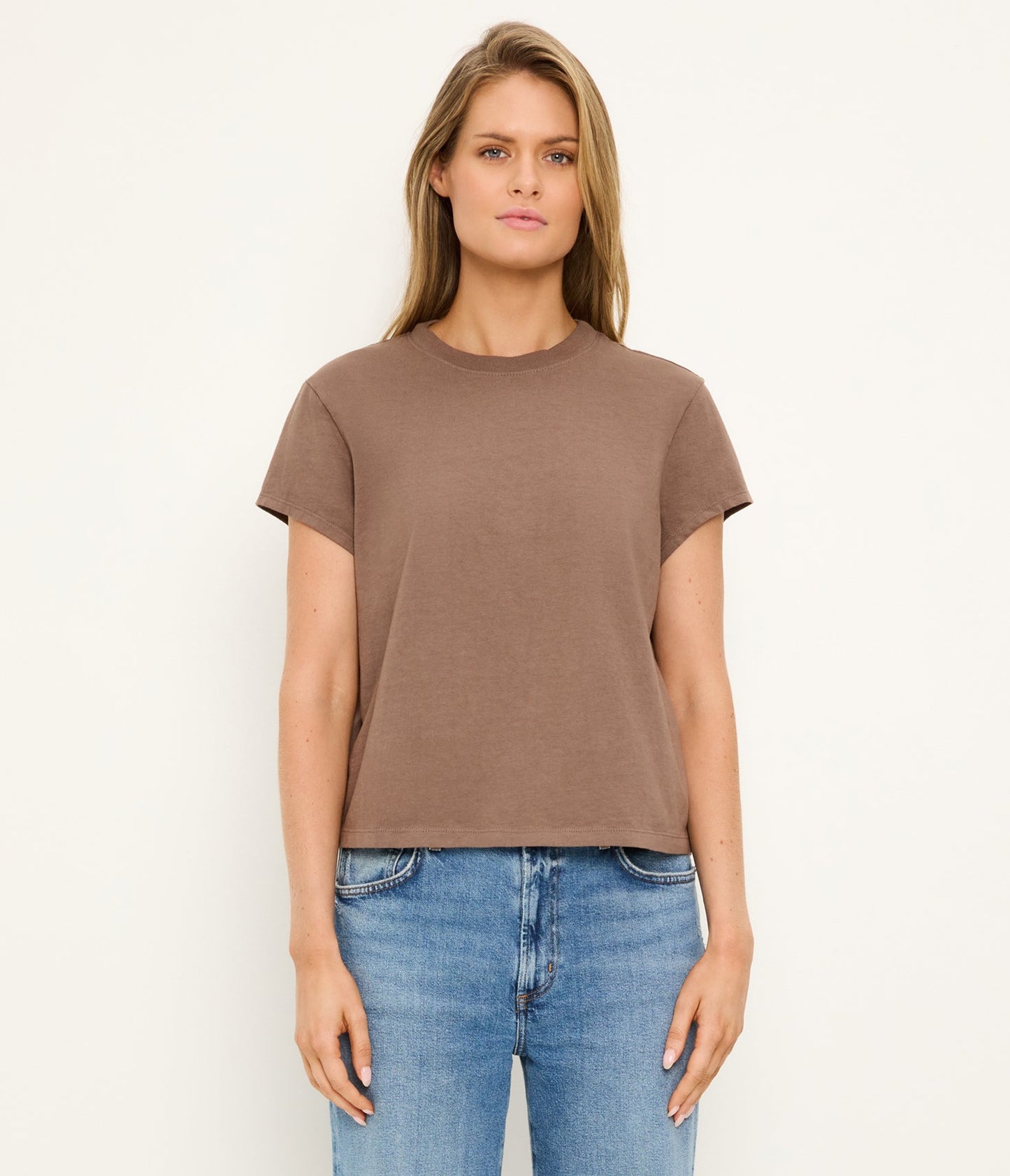 Woman wearing a brown t-shirt and blue jeans on a white background