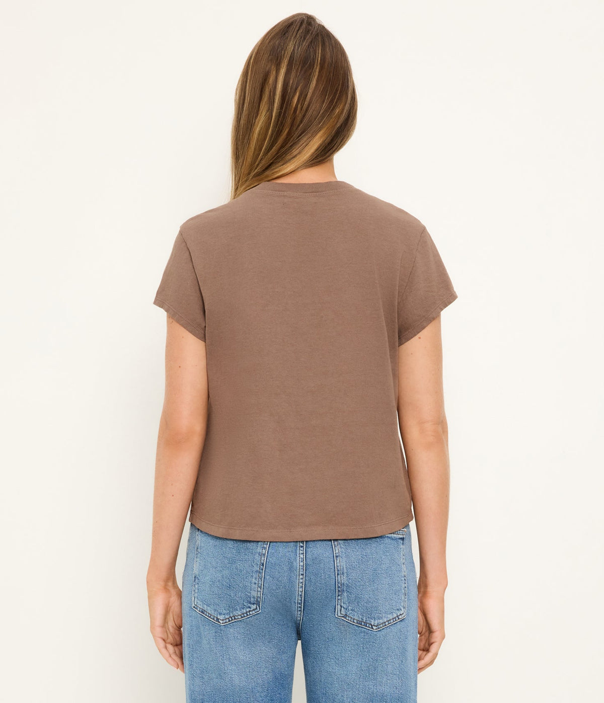 Person wearing a brown t-shirt and blue jeans on a white background