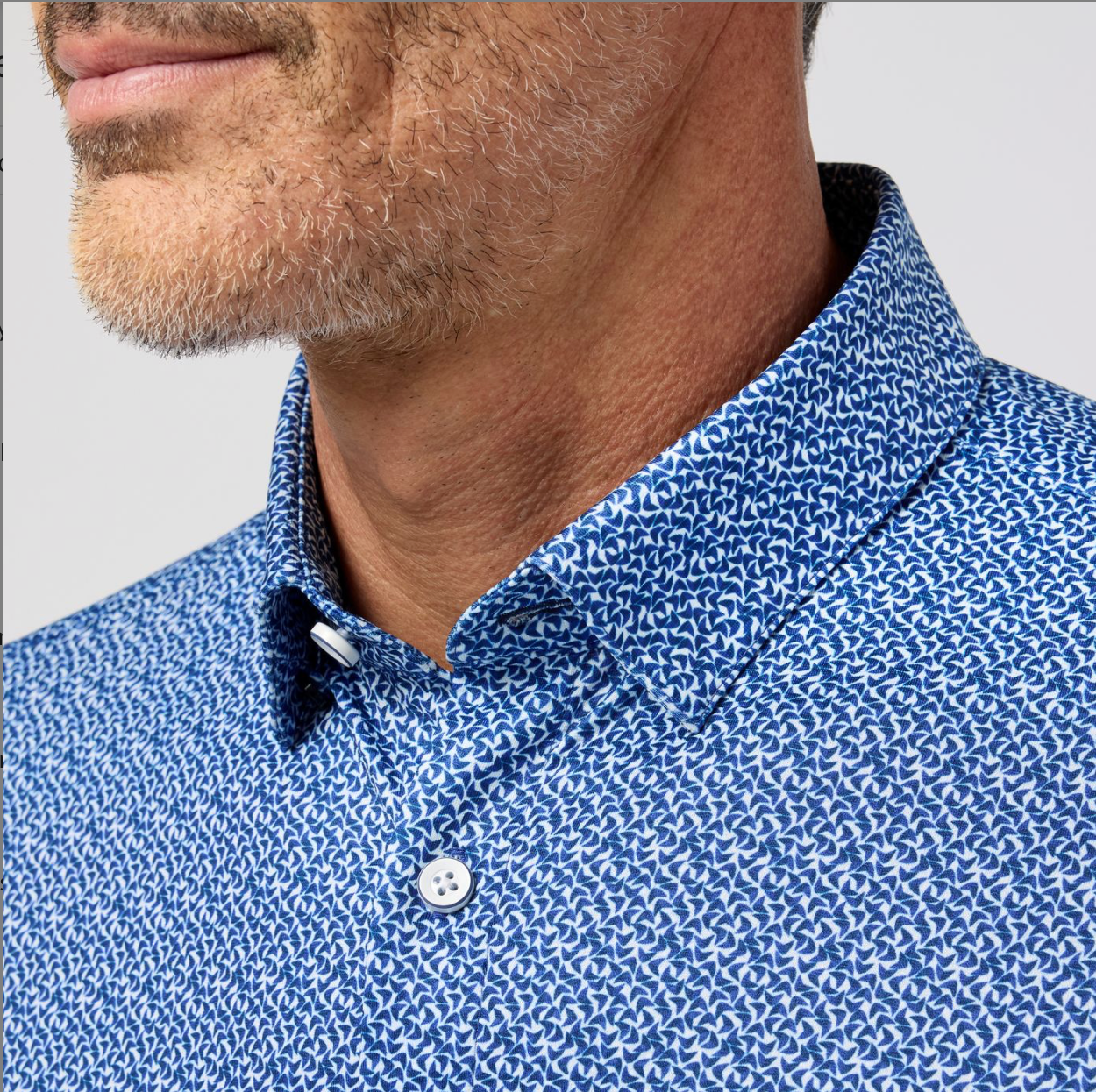 Close-up of a person wearing a blue patterned shirt with a neutral background