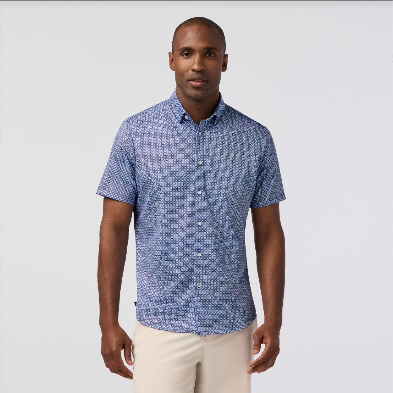 Man wearing a blue patterned shirt and white pants on a light gray background