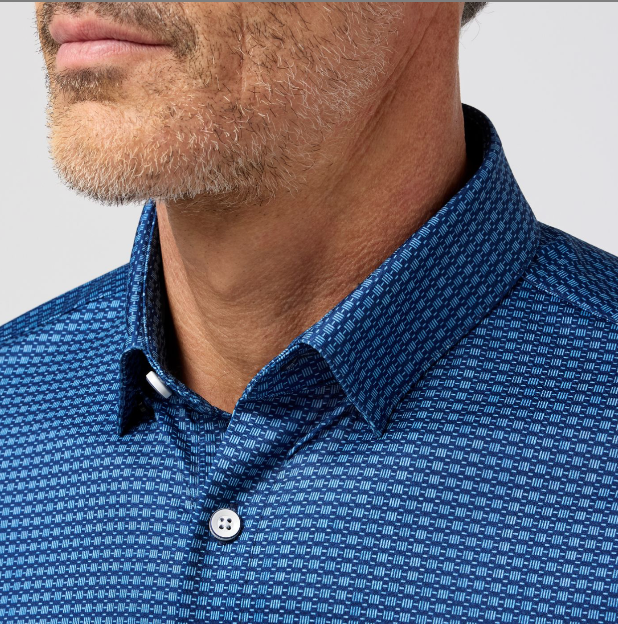 Close-up of a man wearing a blue patterned shirt against a gray background