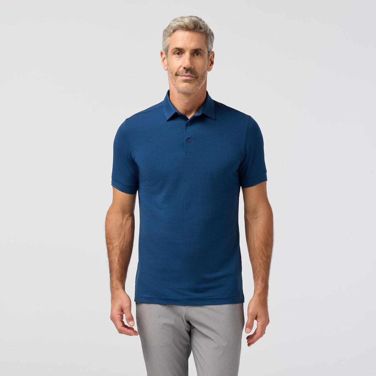 Man wearing a blue polo shirt and gray pants on a light gray background