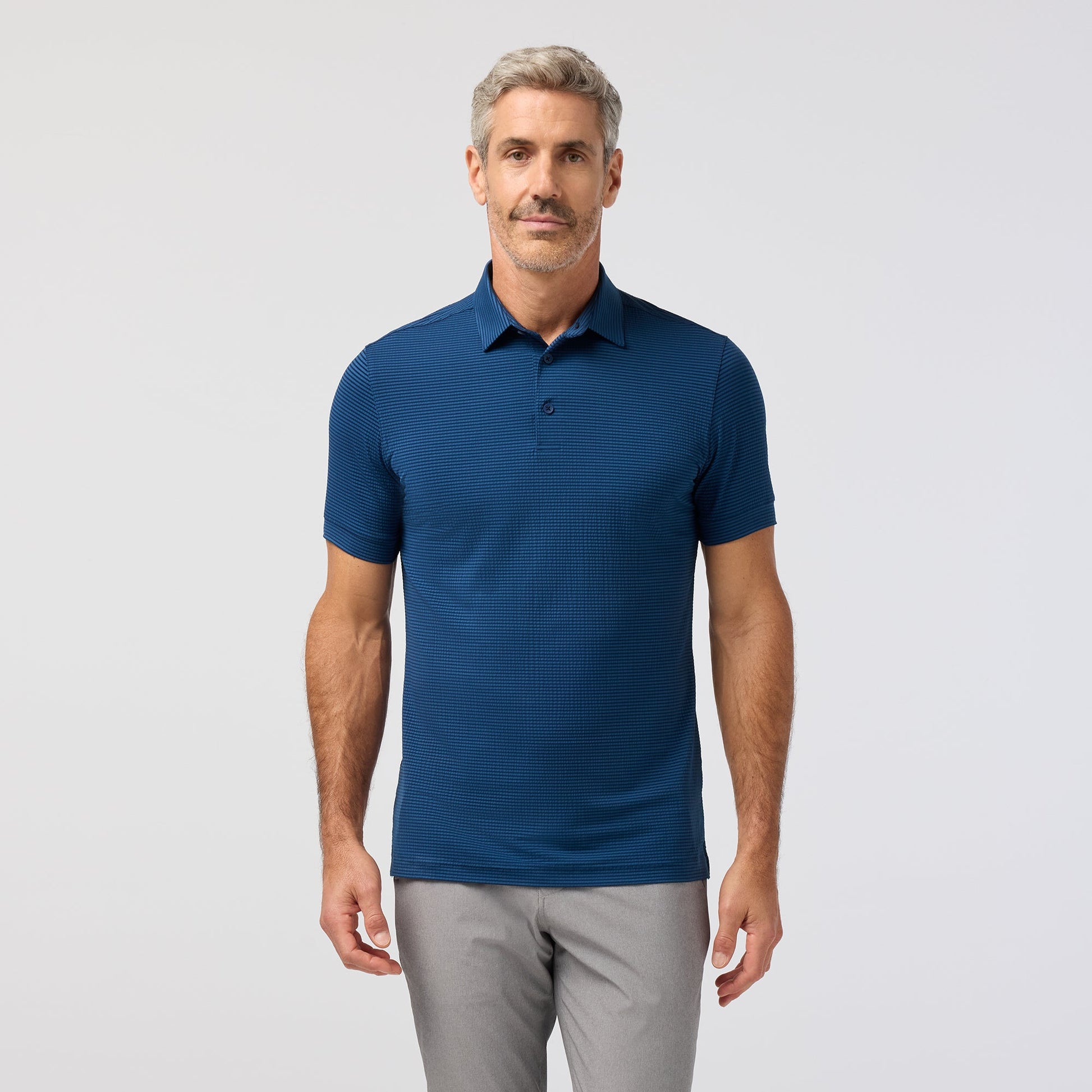 Man wearing a blue polo shirt and gray pants on a light gray background