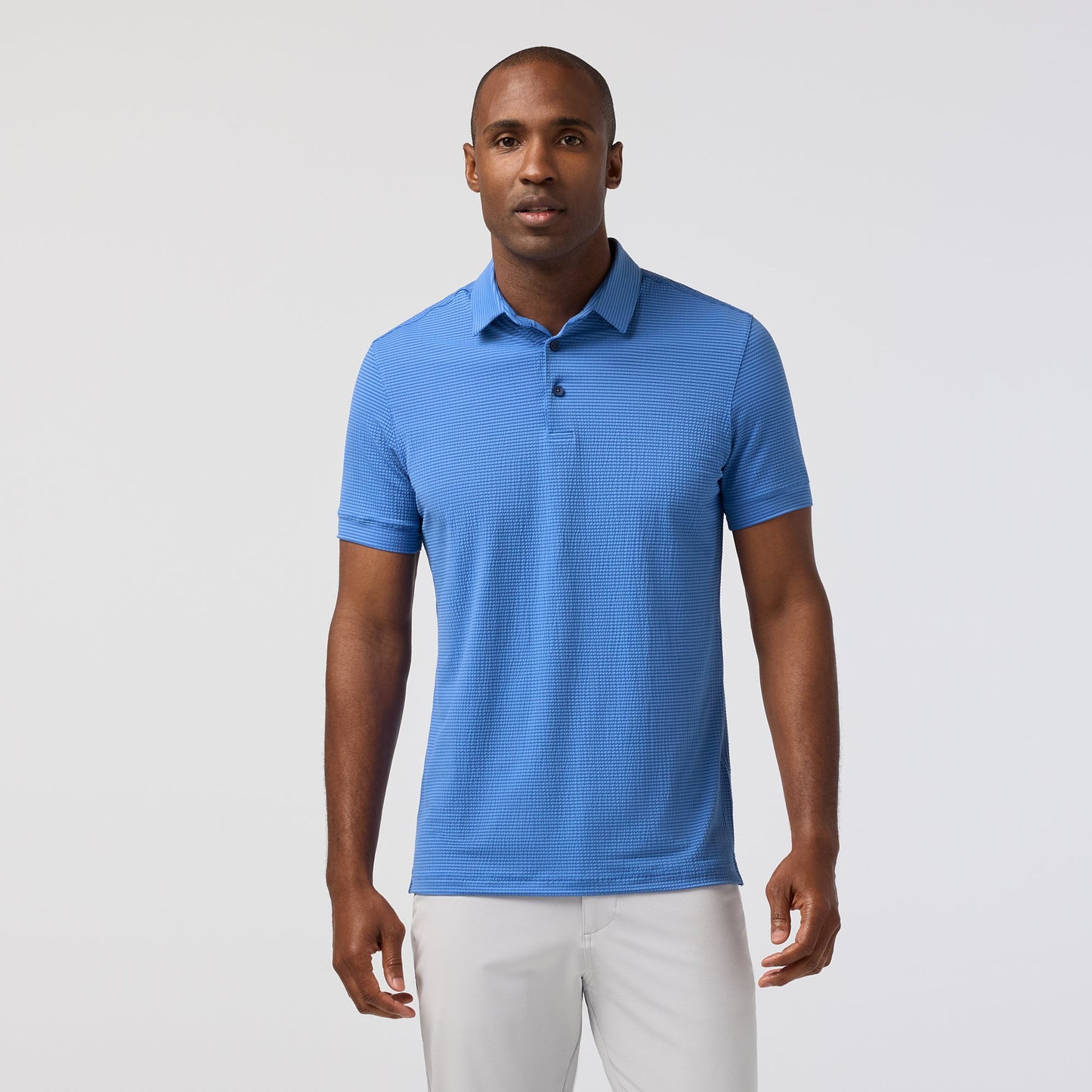 Man wearing a blue polo shirt and white pants on a light gray background