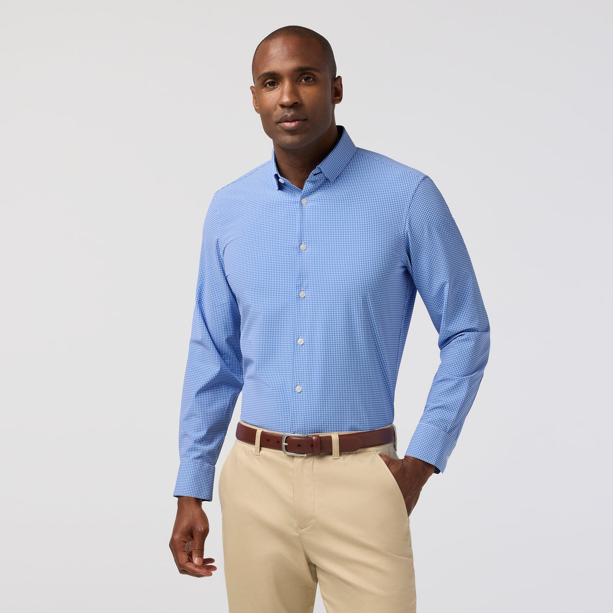 Man wearing a blue patterned shirt and beige pants on a light gray background
