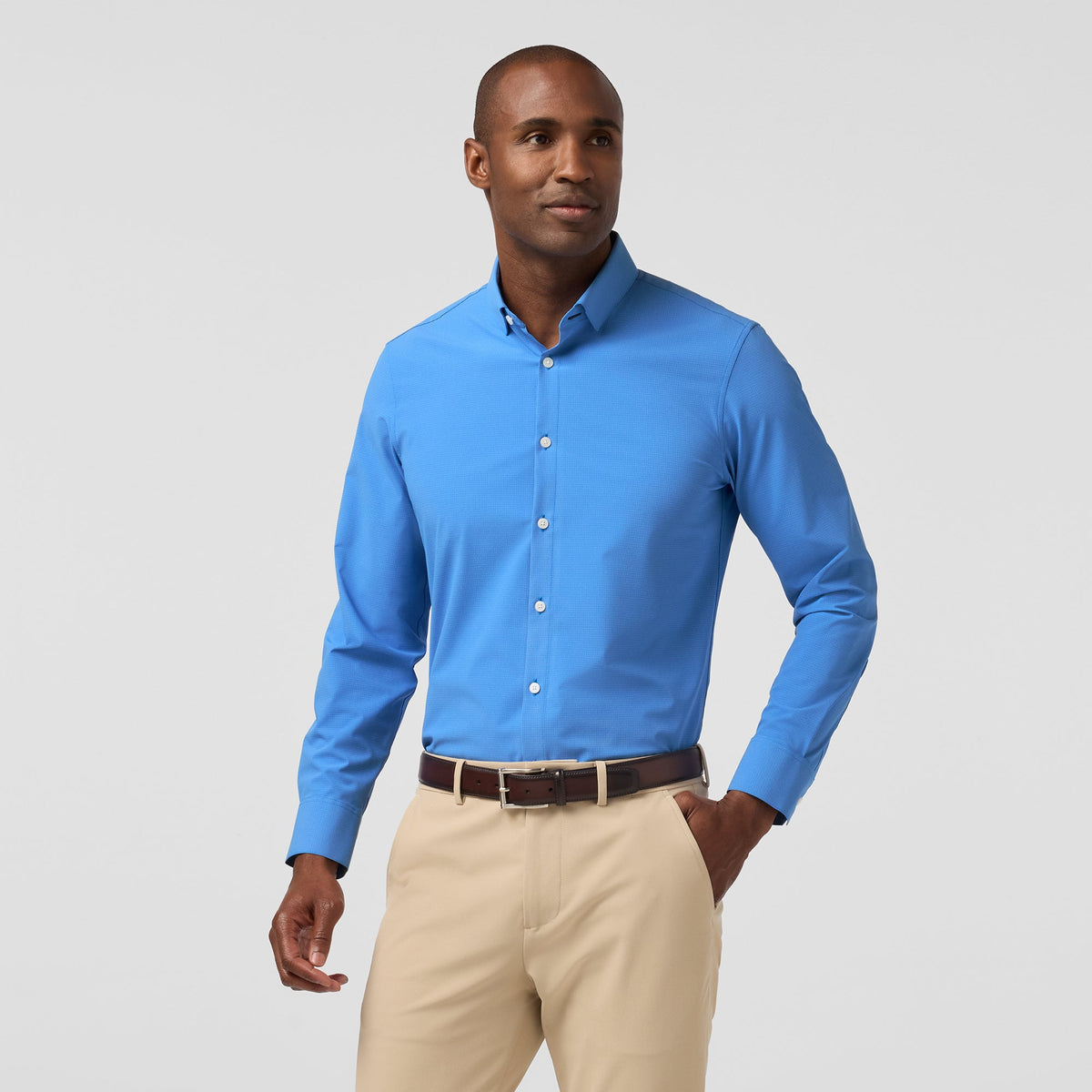 Man wearing a blue shirt and beige pants on a gray background