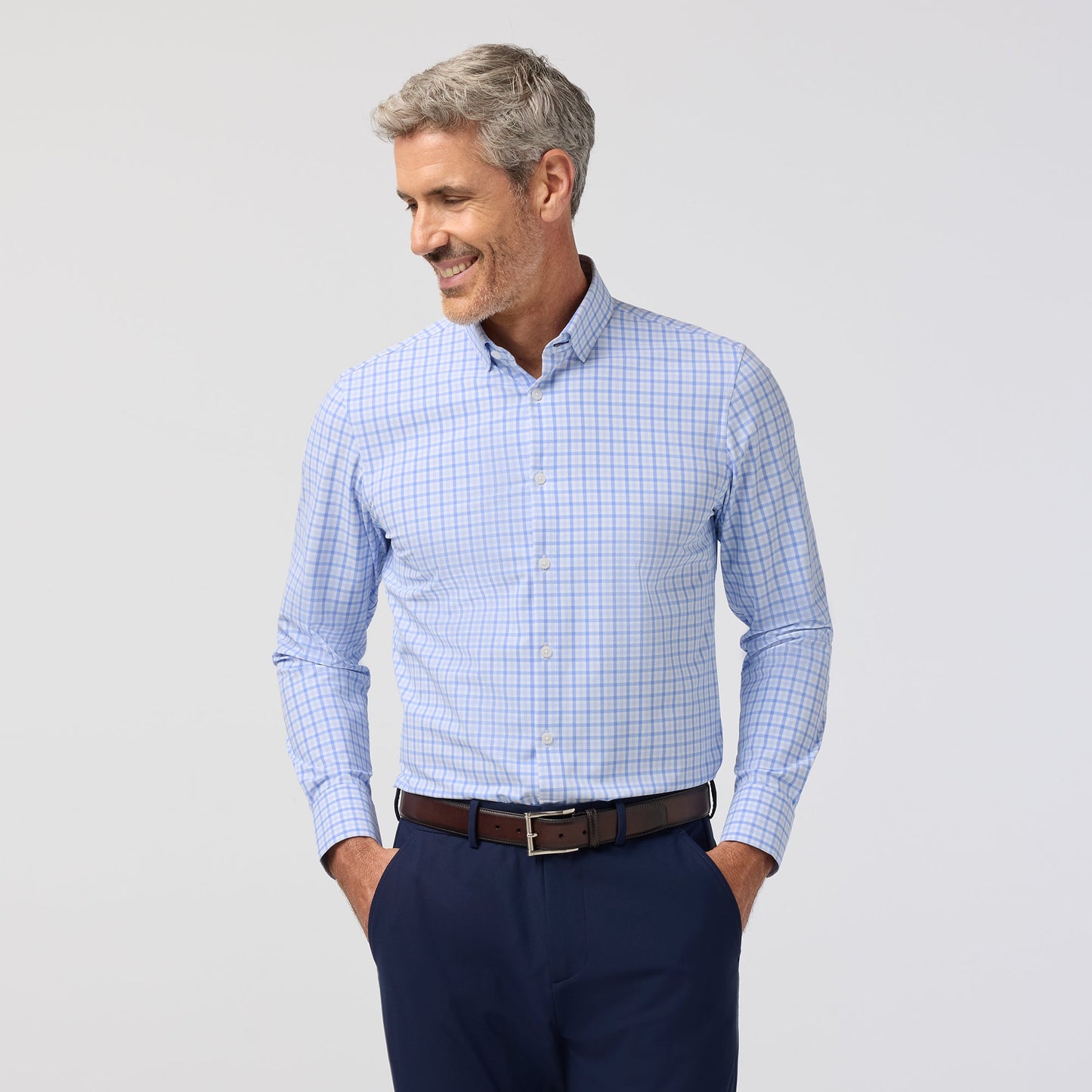 Man wearing a blue checkered shirt and dark pants on a light gray background