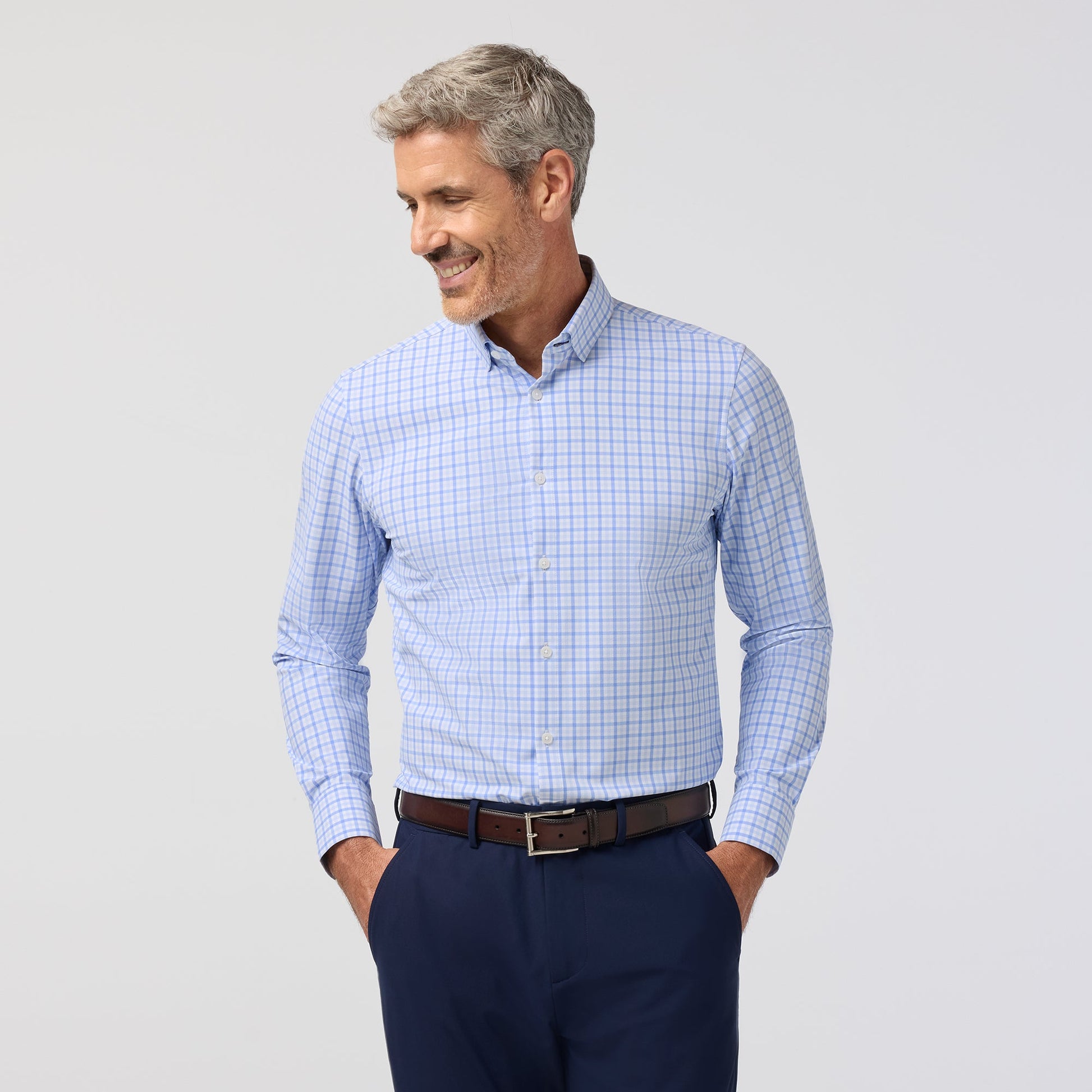 Man wearing a blue checkered shirt and dark pants on a light gray background