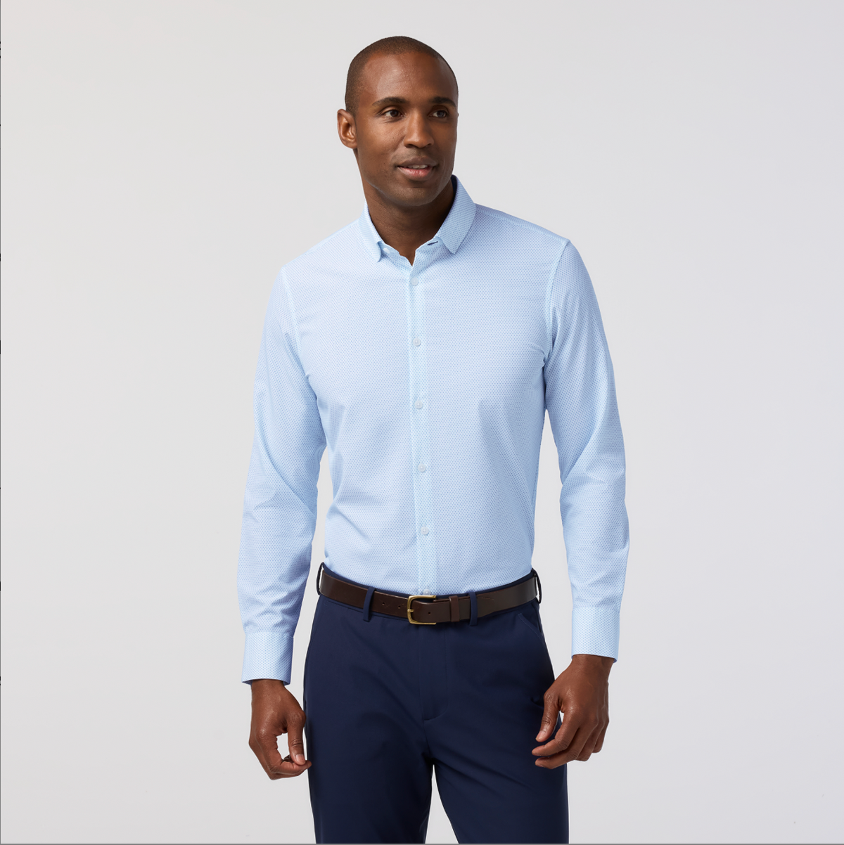 Man wearing a light blue dress shirt and navy pants on a plain background