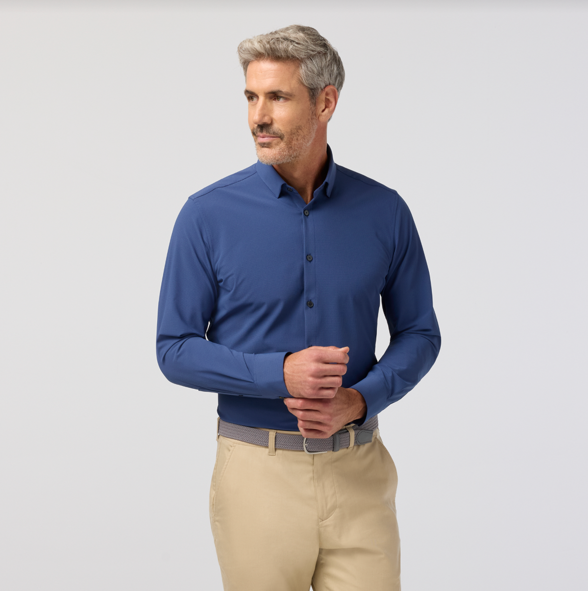 Man wearing a blue long-sleeve shirt and beige pants on a light gray background