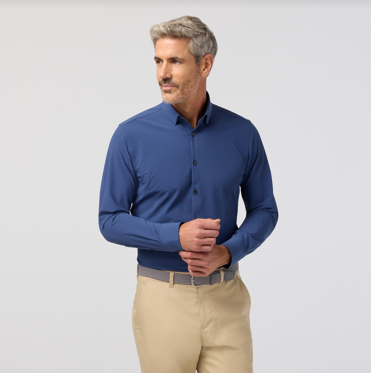 Man wearing a blue long-sleeve shirt and beige pants on a light gray background