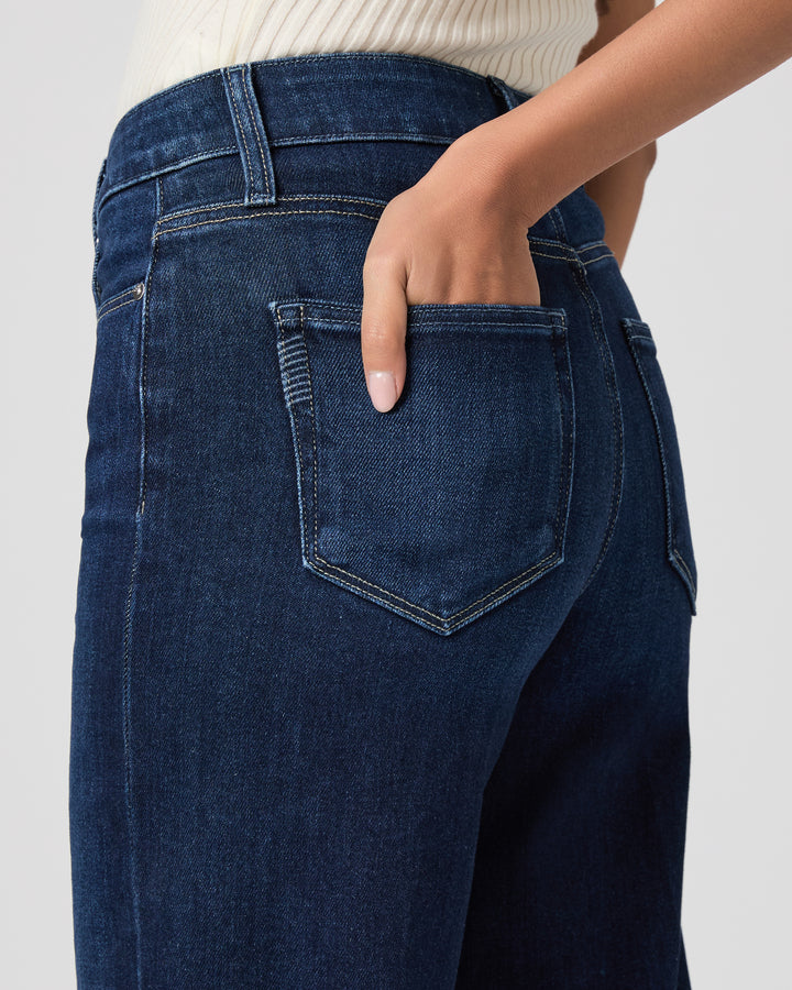 Close-up of dark blue jeans with a hand in the pocket on a light gray background