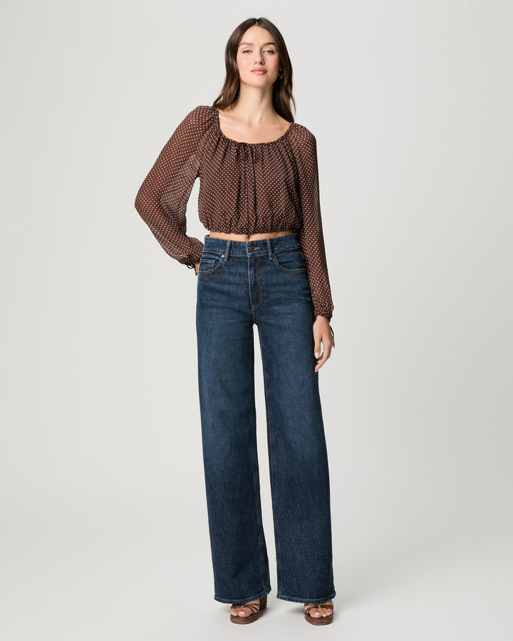 Woman wearing a brown patterned top and blue jeans on a white background