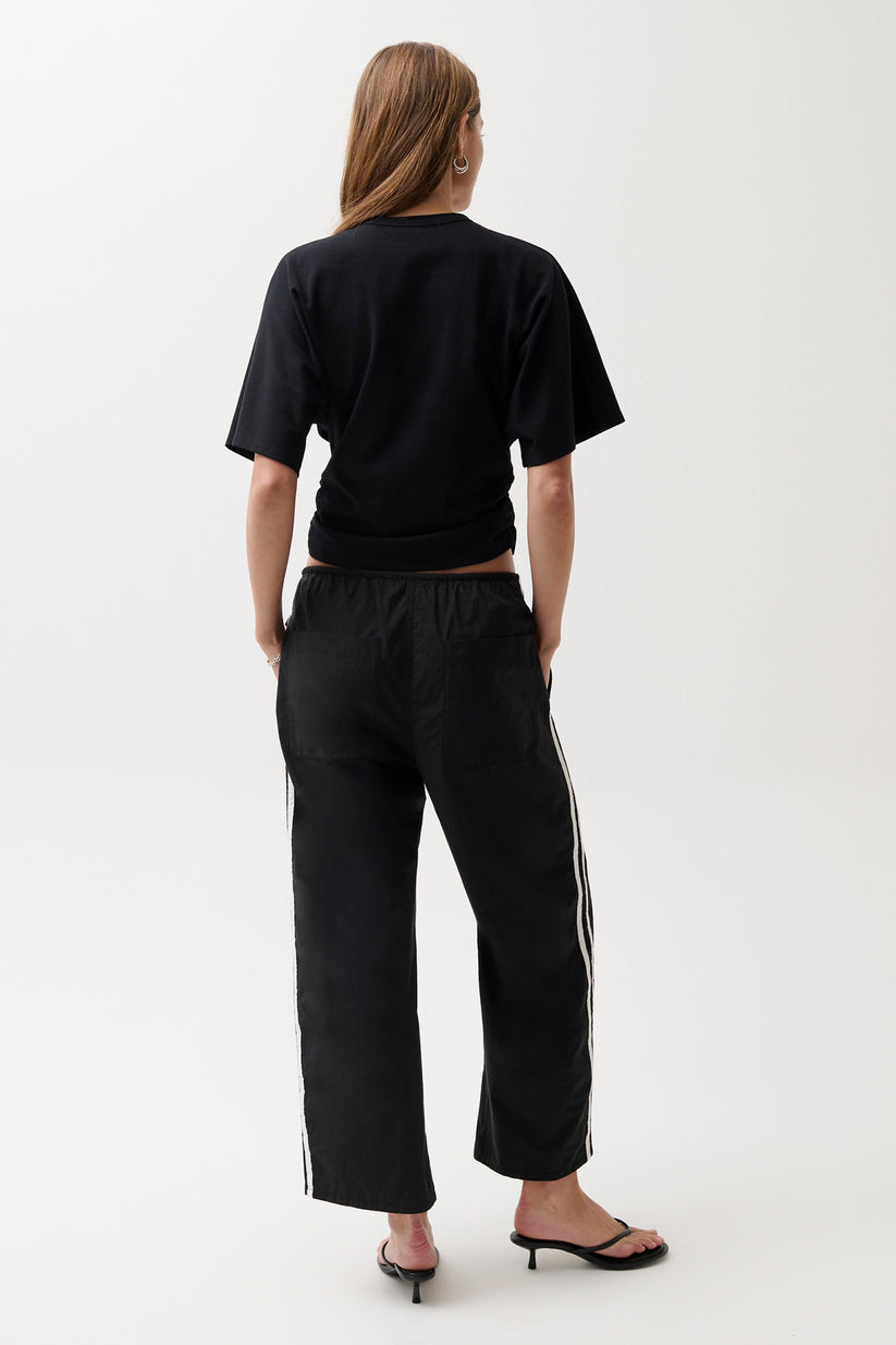 Person wearing a black t-shirt and black pants with white stripes on a white background