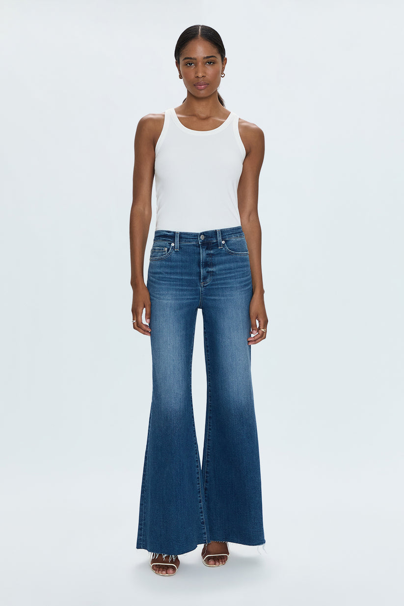 Woman wearing a white tank top and blue flared jeans on a white background