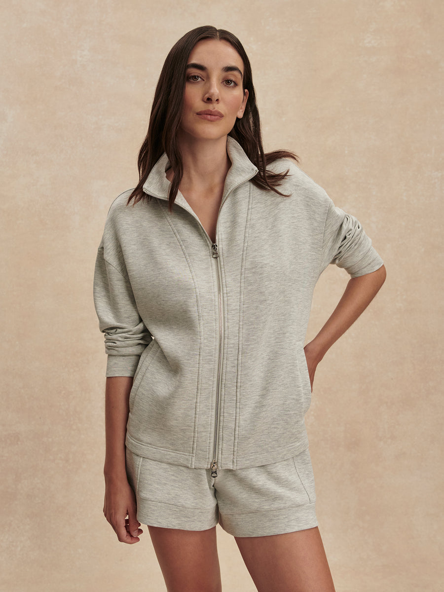 Woman wearing a gray zip-up hoodie and shorts set against a beige background