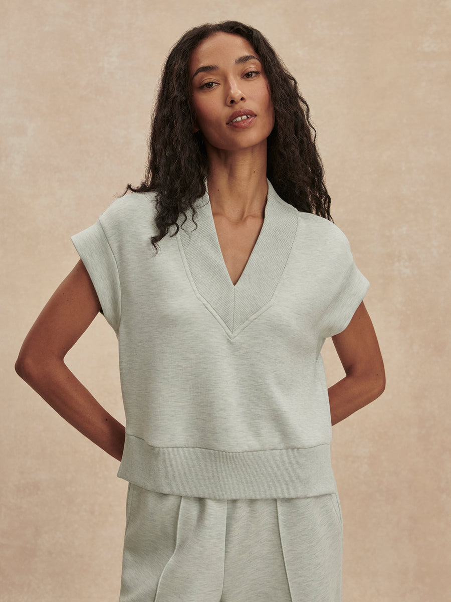 A woman modeling a light sage green knit top and matching bottoms against a textured beige studio backdrop.