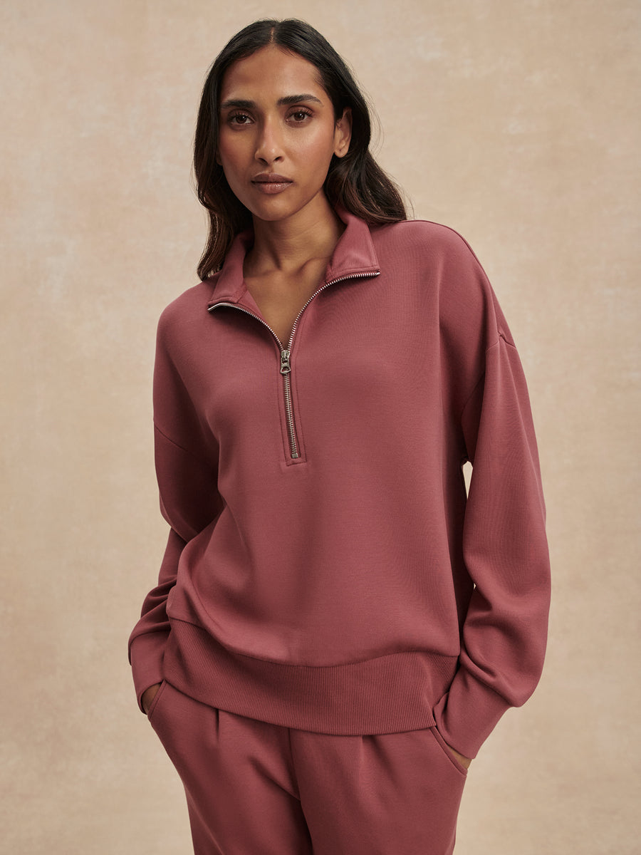 Woman wearing a pink half-zip sweatshirt and pants on a beige background