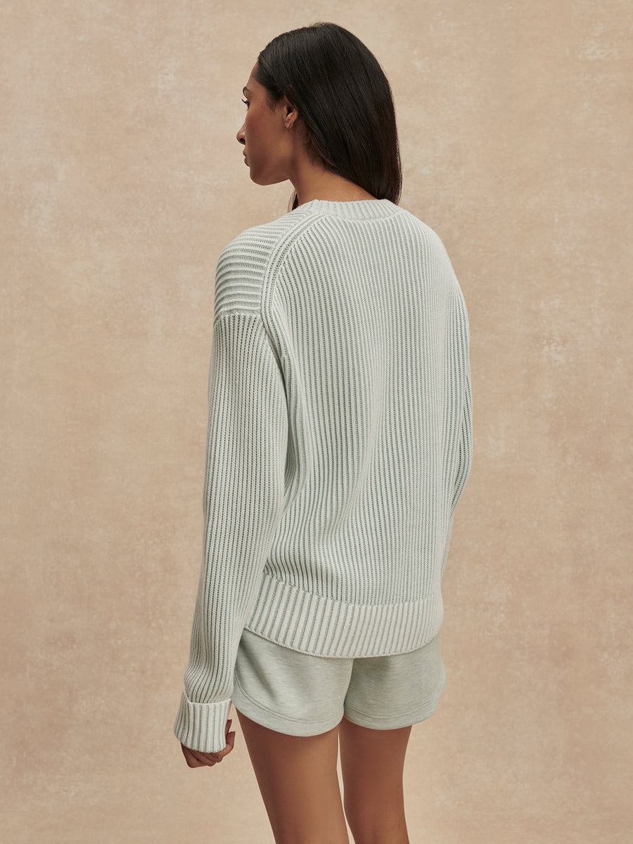 Woman wearing a light green ribbed sweater and shorts against a beige background