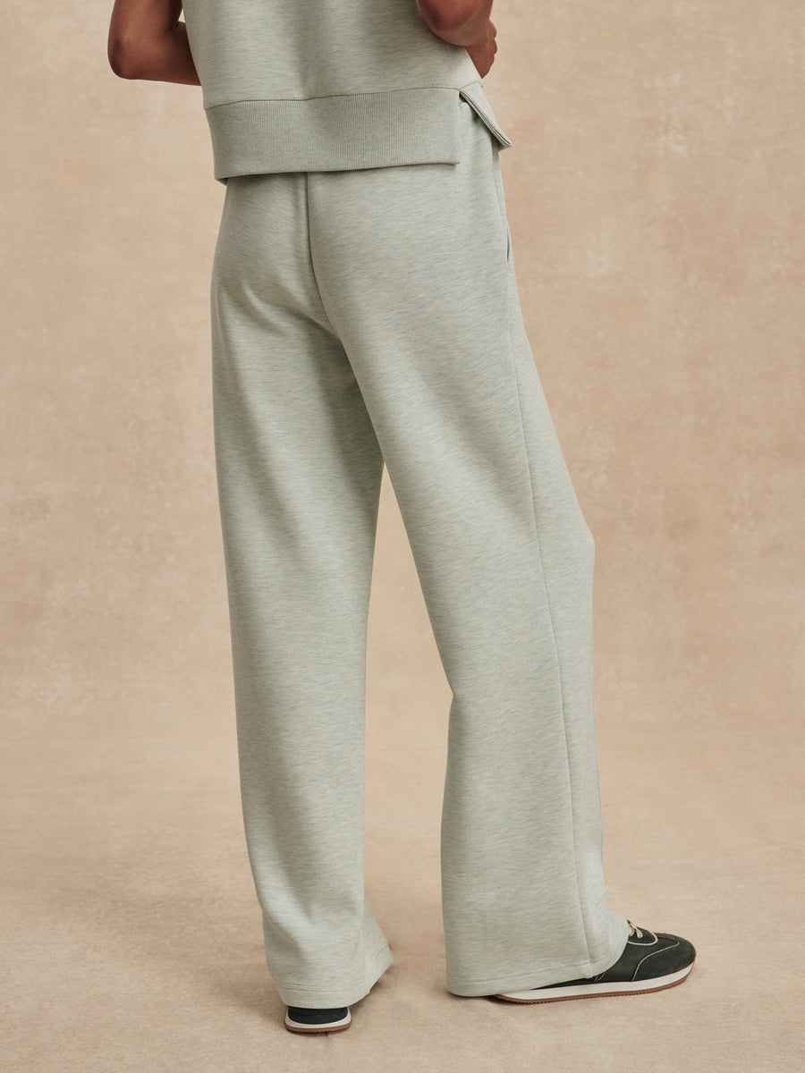A person wearing light sage green wide-leg sweatpants and a matching cropped sweatshirt, shown from the back against a warm beige textured studio backdrop.