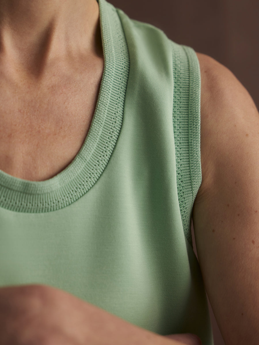 Close-up of a person wearing a light green sleeveless top against a blurred background