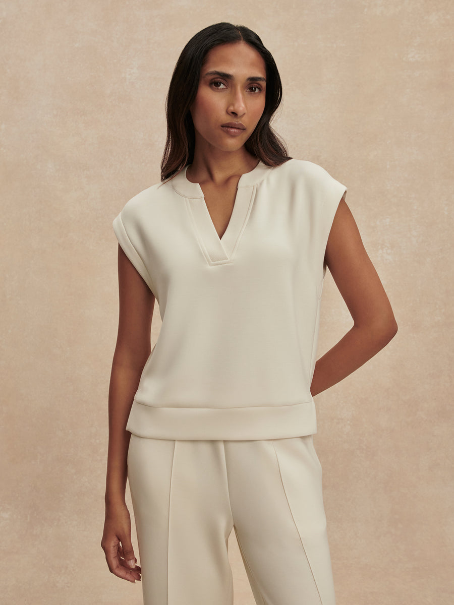 Woman wearing a white sleeveless top and pants against a beige background