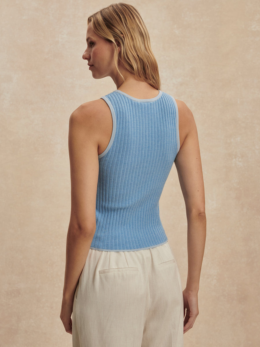 Woman wearing a blue ribbed tank top and beige pants against a beige background