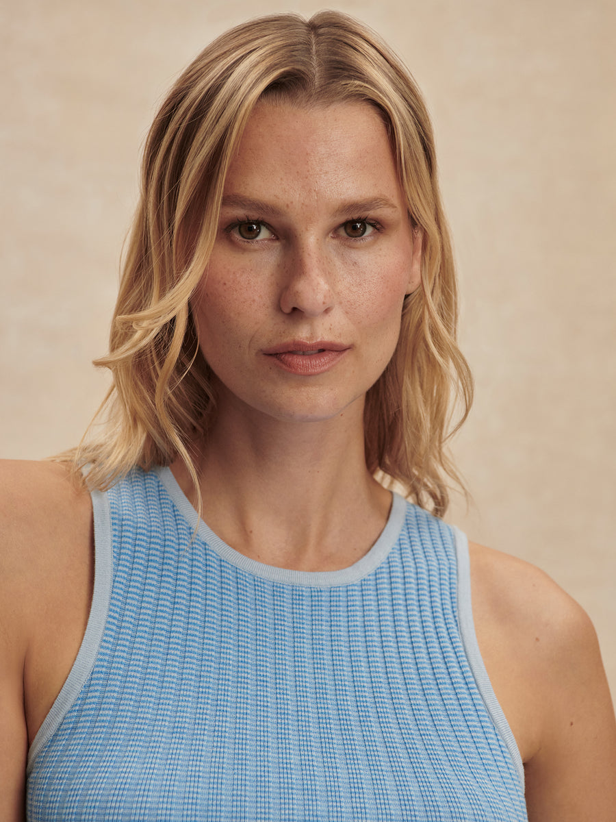 Woman wearing a light blue tank top against a beige background